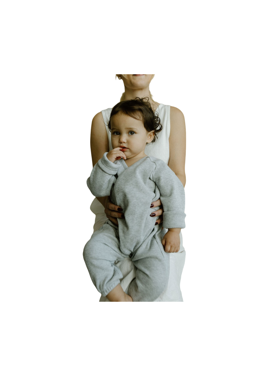 A woman in a sleeveless white dress, made from ethically handmade fabric, cradles a dark-haired child wearing cabane childrenswear's Après Wrap Organic Waffle. The child's hand touches their face as they rest comfortably, while the woman's face isn't visible.