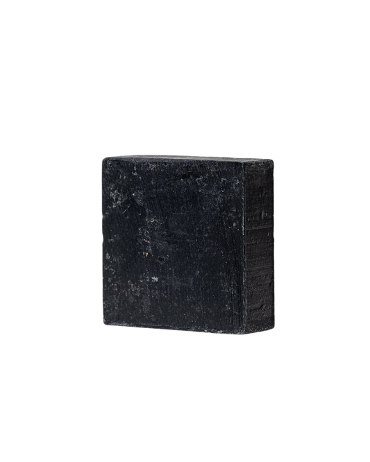 A rectangular black bar of Charcoal Tallow Soap by My Neighbor’s Tallow, featuring a rough, matte texture, is displayed against a plain white background.