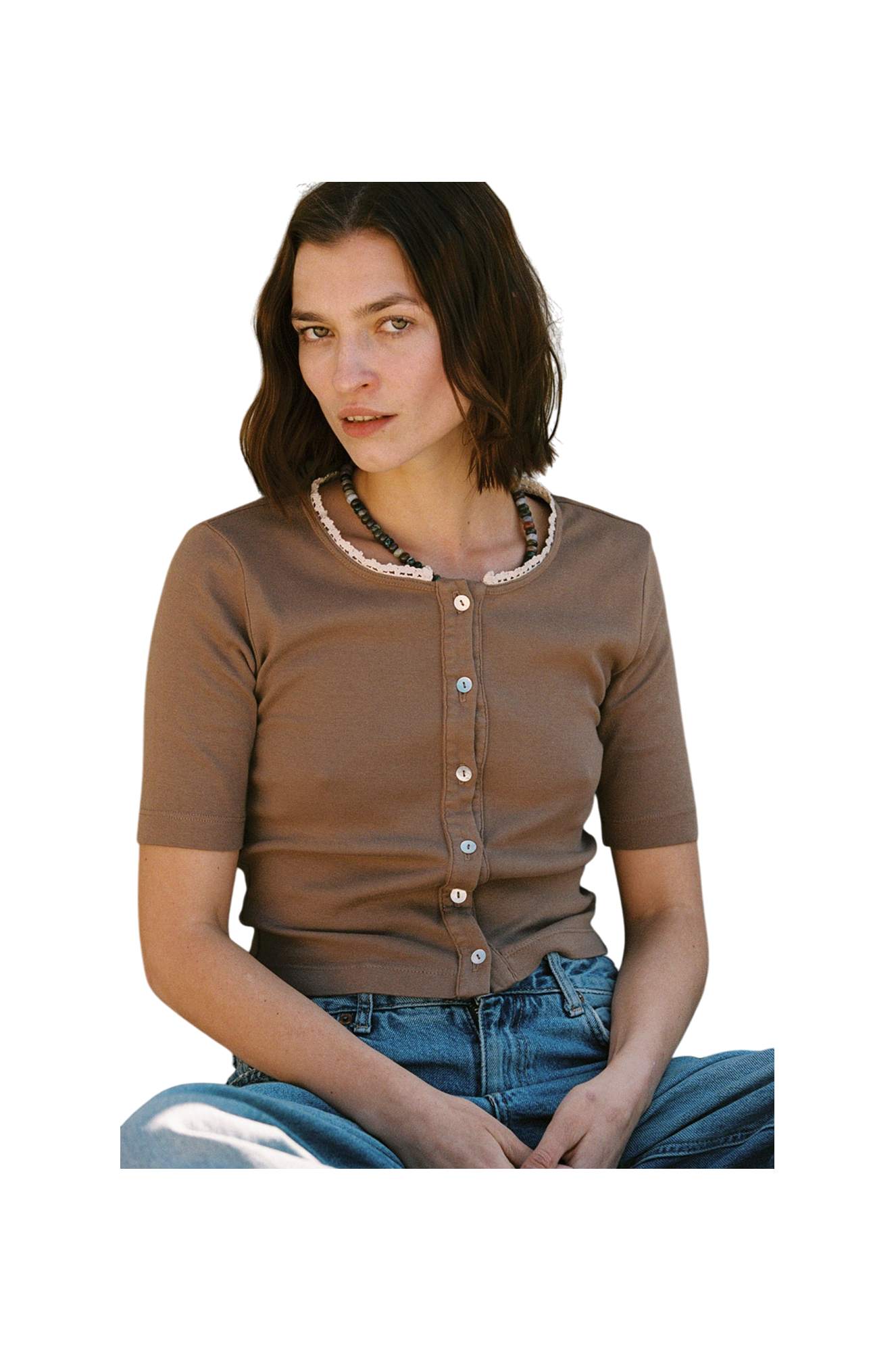 A person with shoulder-length brown hair is seated, looking forward. They're wearing an LA Relaxed Short Sleeve Organic Cardi, paired with blue jeans against a plain white backdrop.