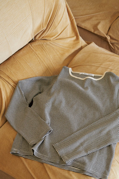 The Organic Stripe Long Sleeve from LA RELAXED, a black and white striped organic cotton shirt with a round neckline, is neatly arranged on a beige sofa adorned with textured light brown fabric and slight wrinkles.