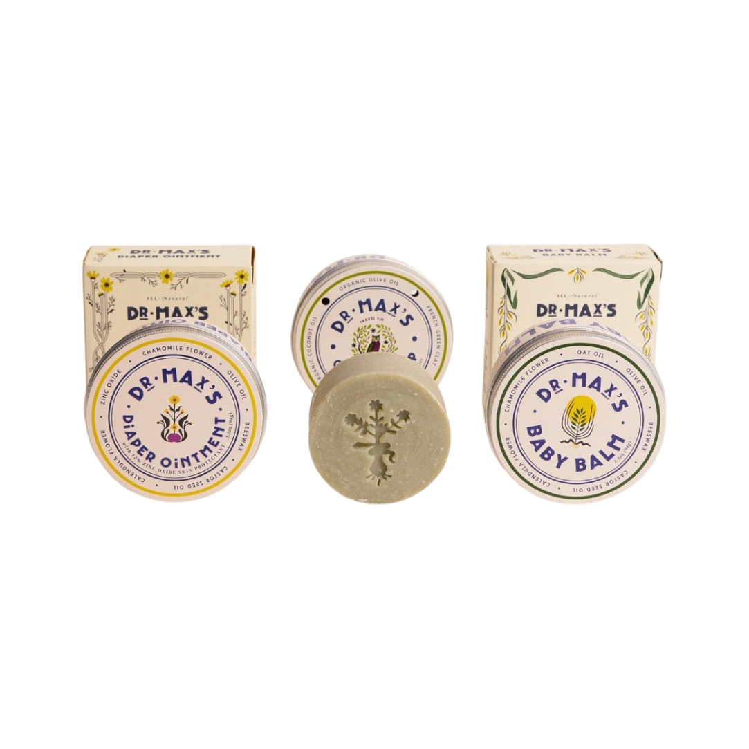 The Dr. Max's Baby Essentials Bundle features vintage-style packaging: two boxes and tins for Baby Balm and Diaper Ointment, plus a round Olive Oil Soap bar with a floral imprint nestled between them.