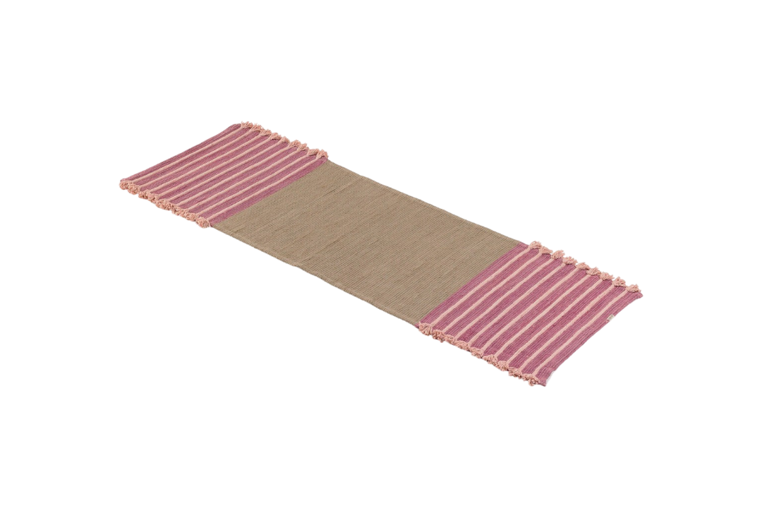 Product: Dark Harda and Sappan Wood Ayurvedic Yoga Mat by Bennd Yoga  
Description: A woven yoga mat crafted from organic materials showcases a beige center with pink striped fringed edges, presented on a plain background.