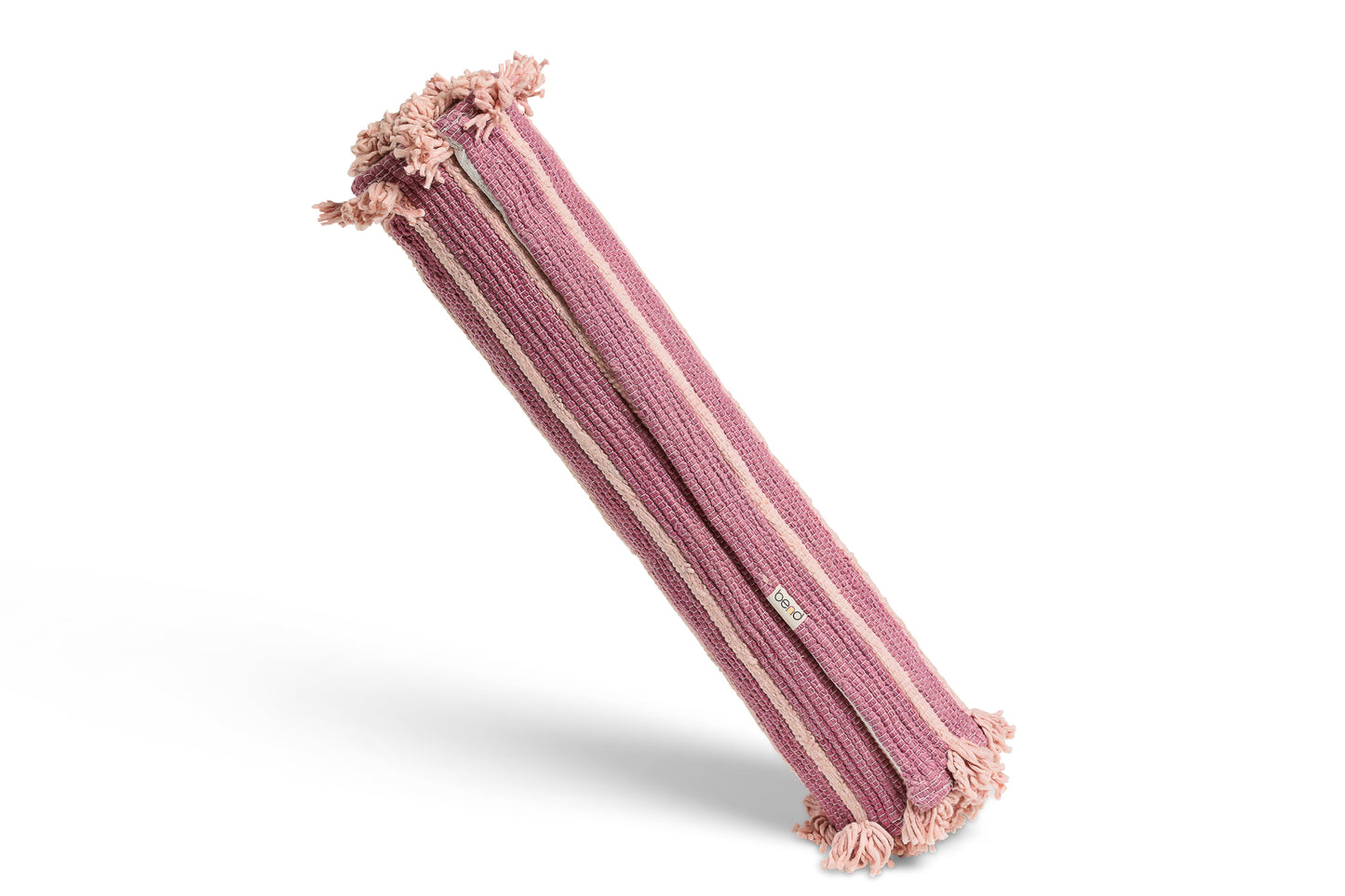 A Dark Harda and Sappan Wood Ayurvedic Yoga Mat from Bennd Yoga, featuring a pink and mauve striped pattern with tassels on both ends, stands upright against a plain white background.