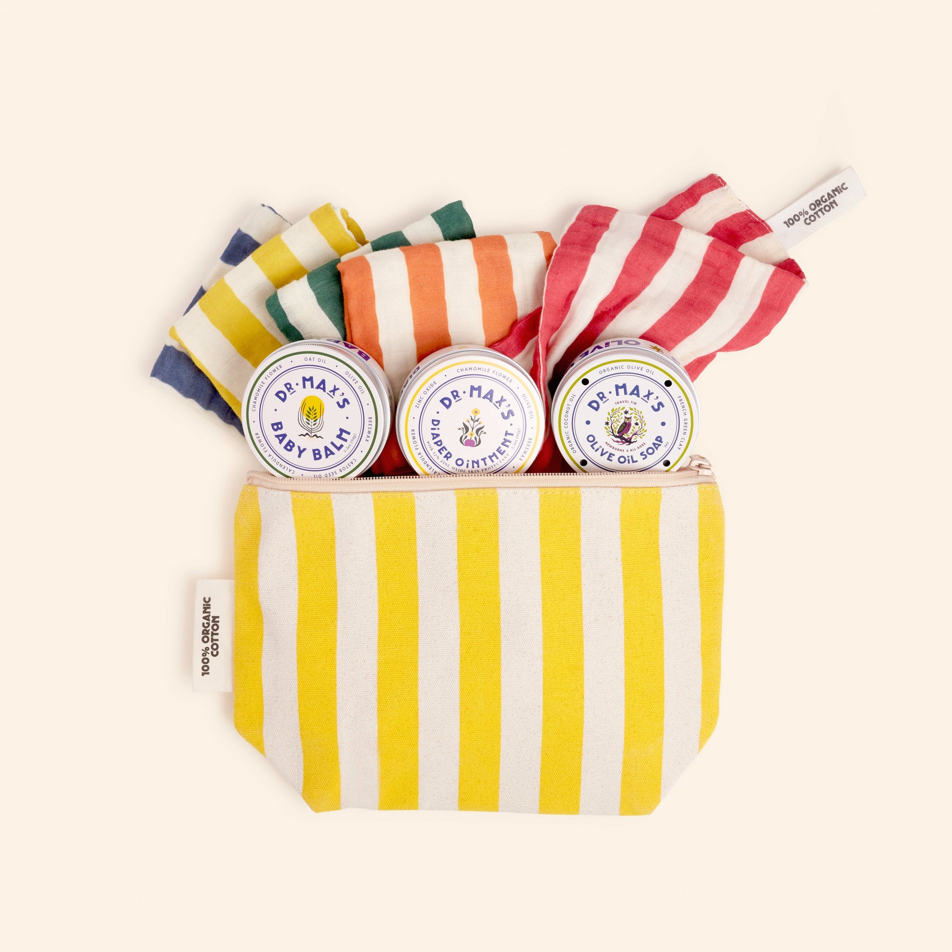 The Dr Maxs Newborn Gift Box features a yellow and white striped pouch with three Baby Balm tins and three vibrant striped fabric items in shades of yellow, green, orange, and red.