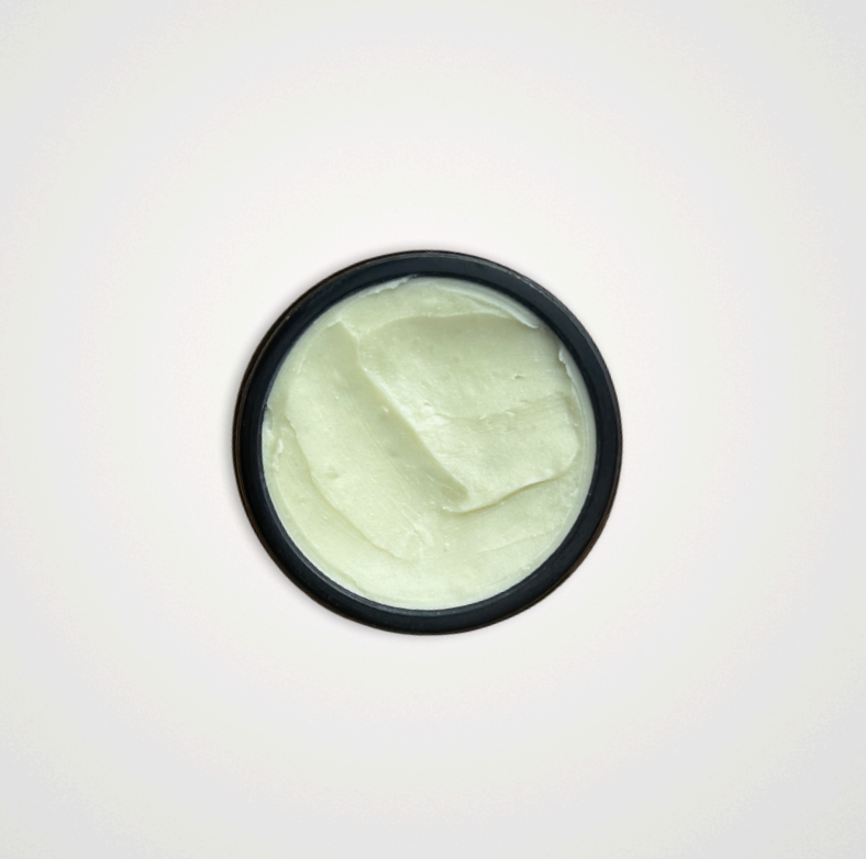 A round, black container of Wild Mamas Earth, Whipped & Sky 3.16oz tallow balm filled with smooth, pale green whipped balm, viewed from above against a plain white background.