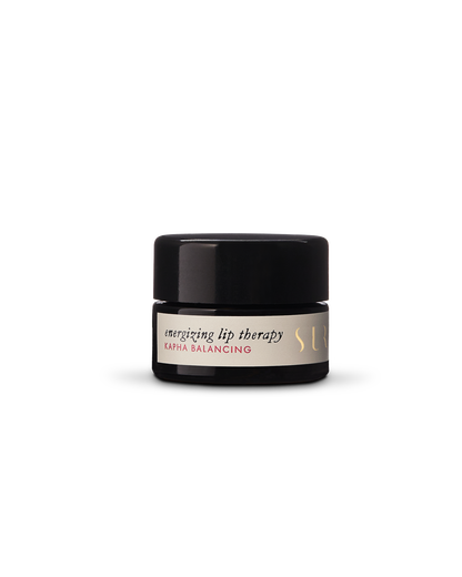 A small black jar featuring a white label with the text "Energizing Lip Therapy - Kapha Balancing" by Surya. The natural lip therapy is packaged in a jar with a black lid and gold embossed text on the label, set against a neutral background.