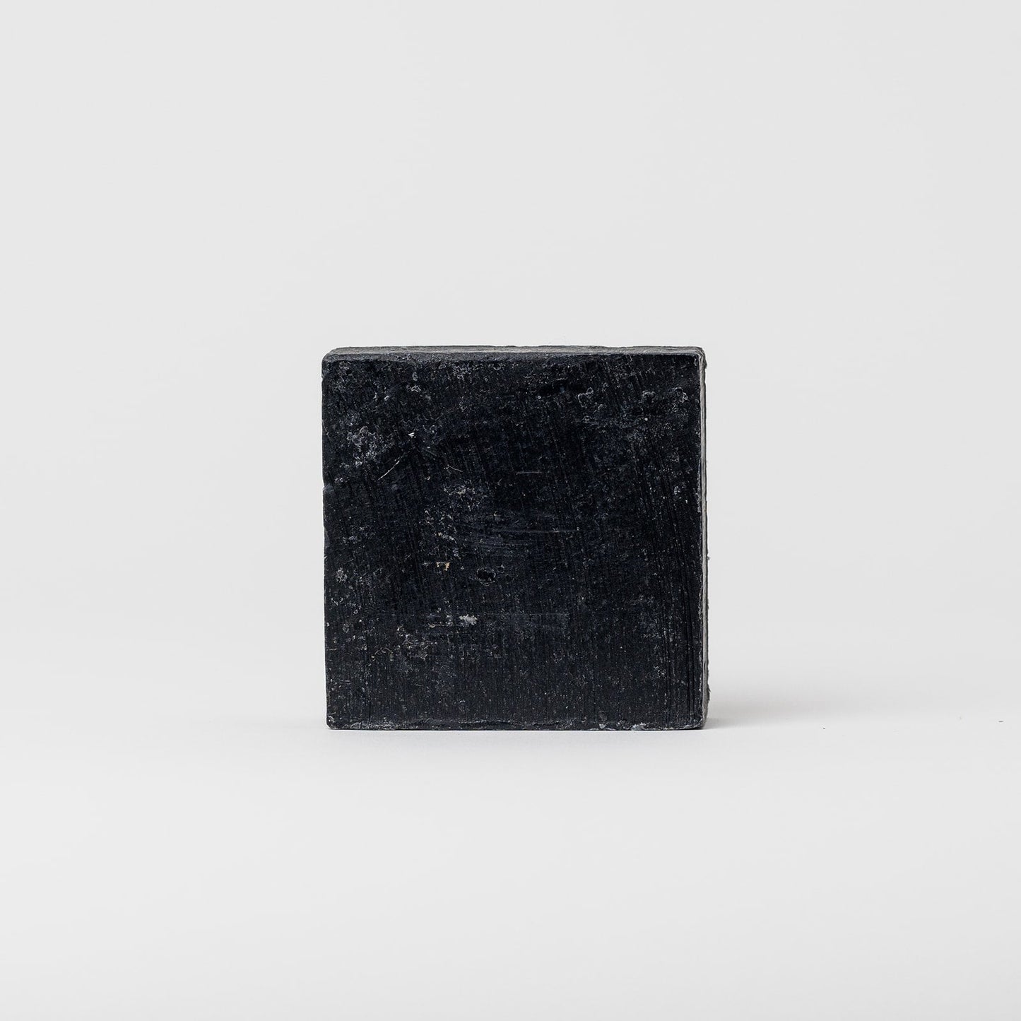 A rectangular, black Charcoal Tallow Soap by My Neighbor’s Tallow stands upright on a plain, light gray background.
