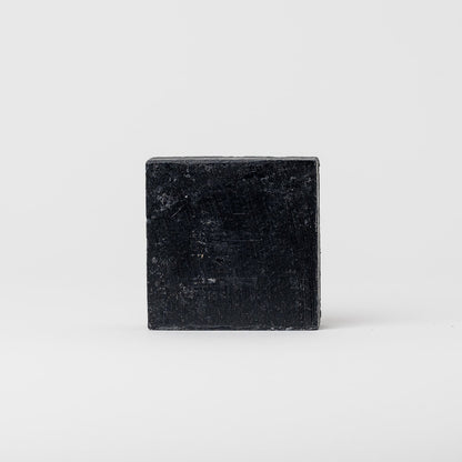 A rectangular, black Charcoal Tallow Soap by My Neighbor’s Tallow stands upright on a plain, light gray background.