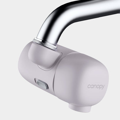 A Canopy Faucet Filter by Canopy is attached to a silver faucet, featuring a sleek, light gray design, set against a plain white background.