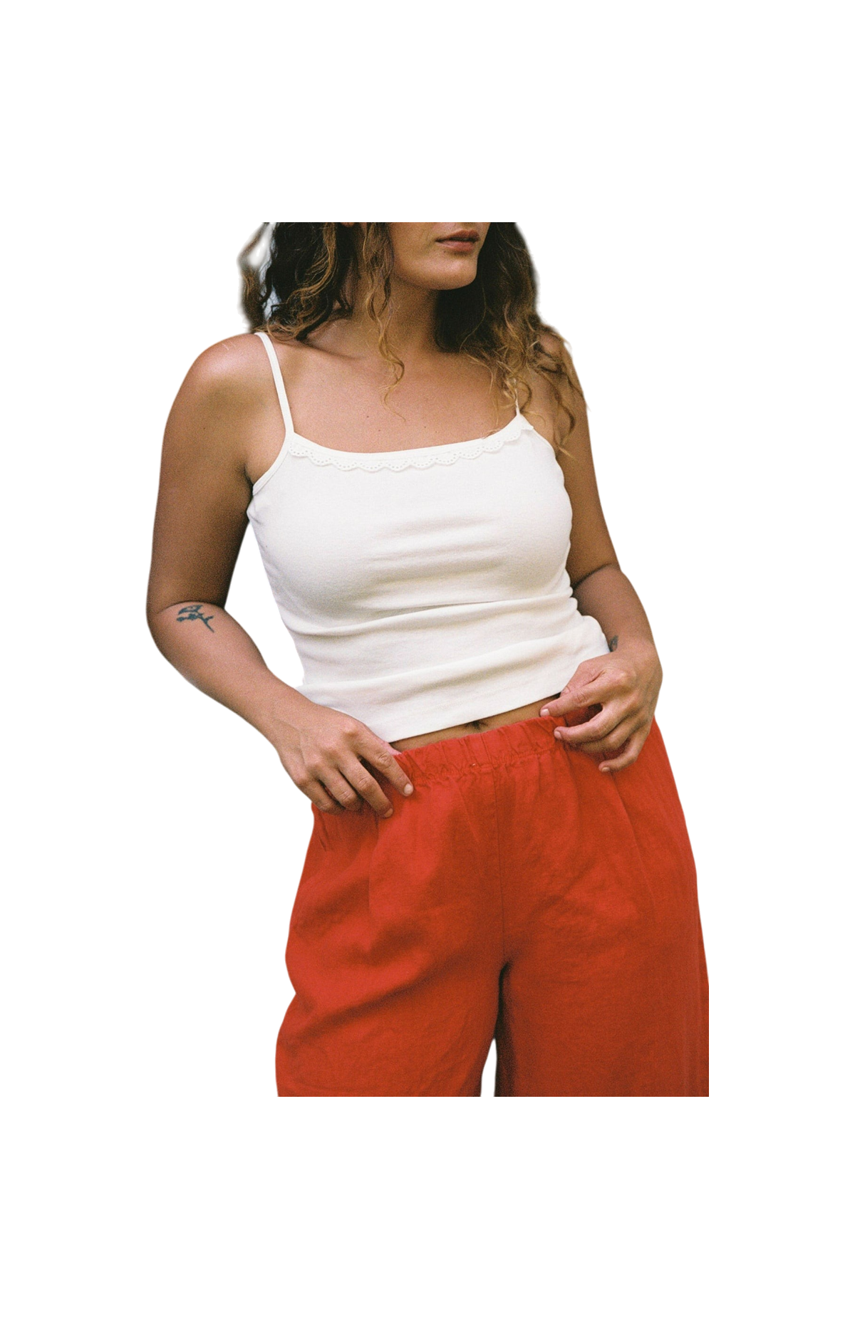 Cream -
A person with wavy hair models the LA RELAXED Frill Camisole paired with loose red pants, posing with one hand on their waist against a plain black background.