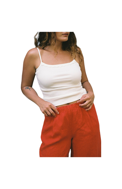 Cream -
A person with wavy hair models the LA RELAXED Frill Camisole paired with loose red pants, posing with one hand on their waist against a plain black background.