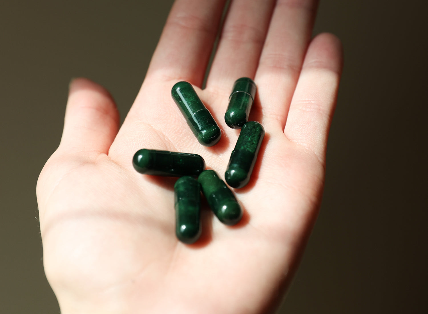 A hand holds several dark green Gut Therapy Supplement capsules from Juna, rich in probiotics, against a neutral background.