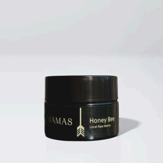 A small, dark container labeled "Wildly Nourishing Bison Tallow Balm - Raw Honey" by Wild Mamas, featuring a gold arrow design, rests on a white surface against a simple light background.