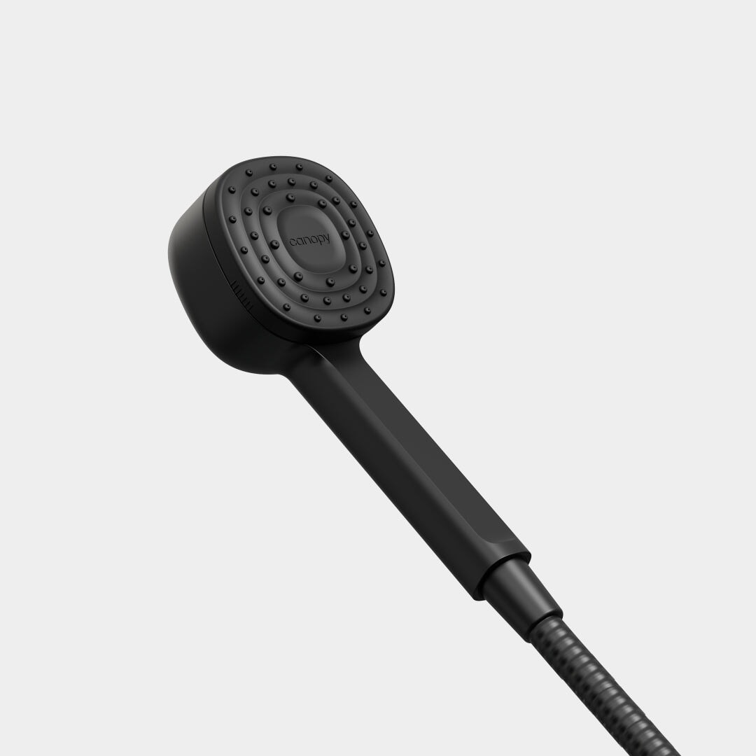 The Canopy Handheld Filtered Showerhead features a sleek black design with a square, rounded-edge nozzle and small, evenly spaced water holes. A flexible hose completes the set, all shown against a plain gray background.
