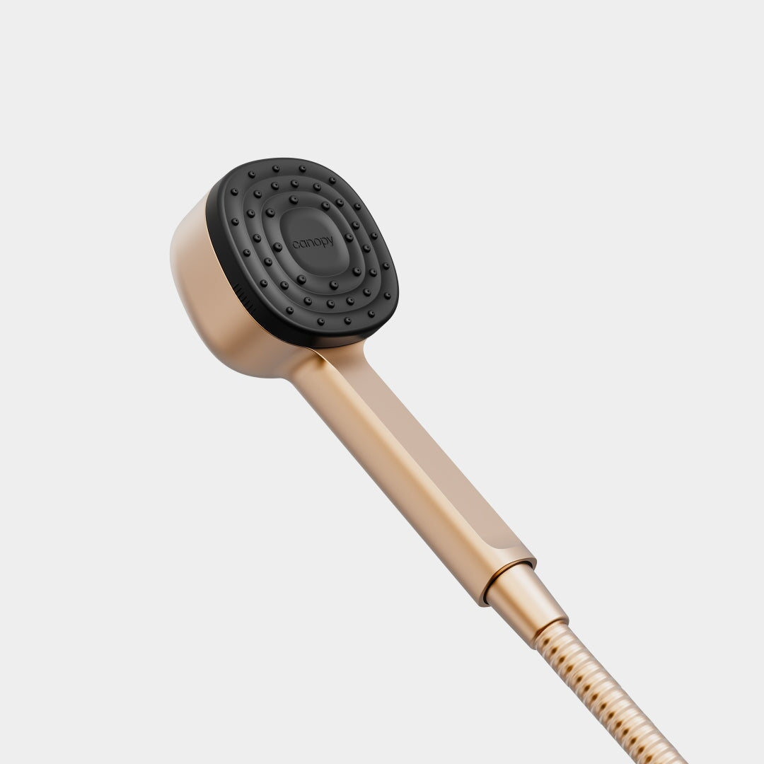 The Canopy Handheld Filtered Showerhead features a matte gold handle and black square spray face, attached to a matching hose, creating a modern look that stands out against a plain white background.