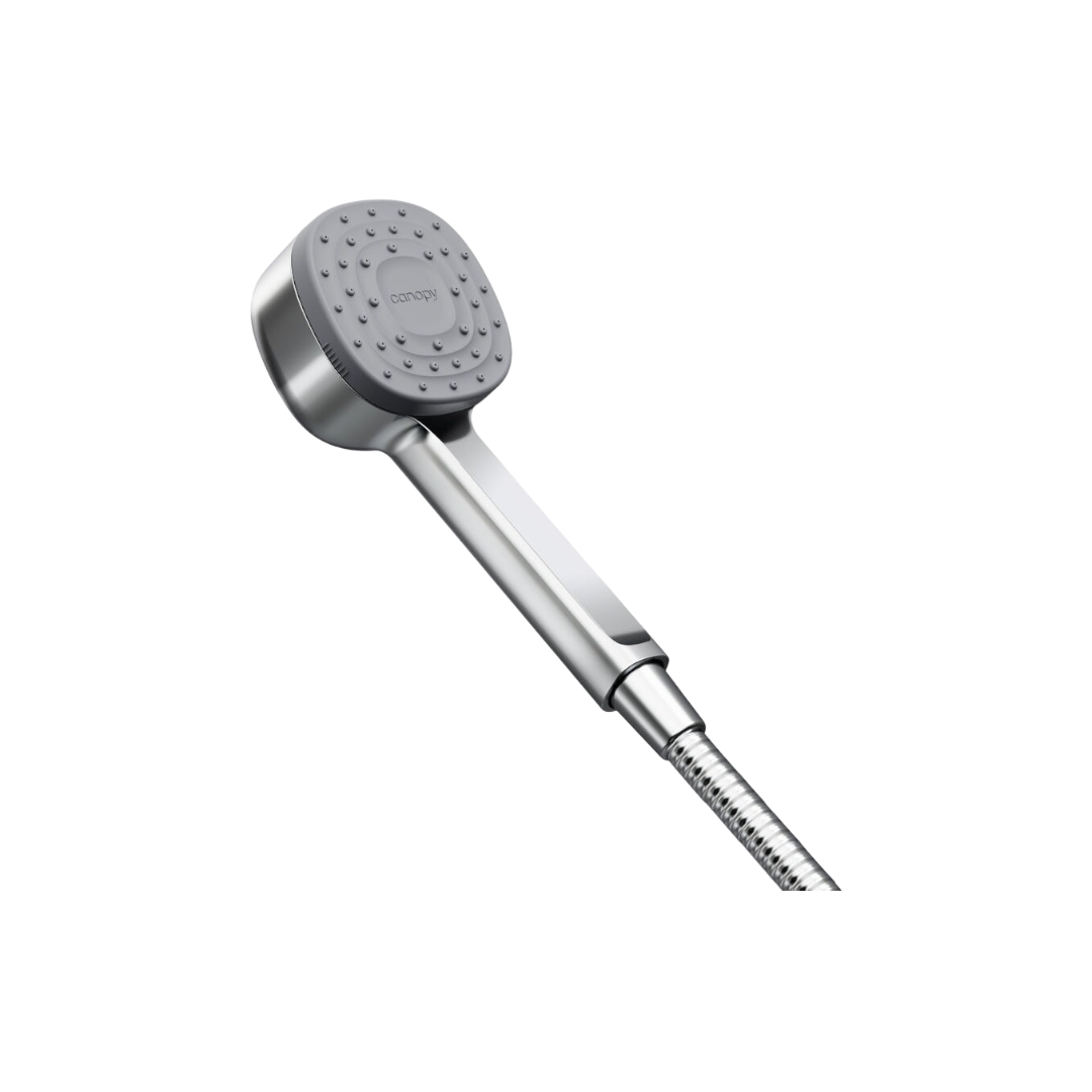 The Canopy Handheld Filtered Showerhead features a gray square face and chrome handle, attached to a flexible metal hose. It removes chlorine to support healthy skin and hair, shown isolated against a black background.