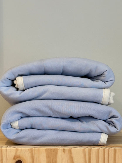 An indigo BABY BLANKET by cabane childrenswear is neatly folded, featuring a hand-quilted design with white edges, resting on a wooden surface against a plain light gray background.