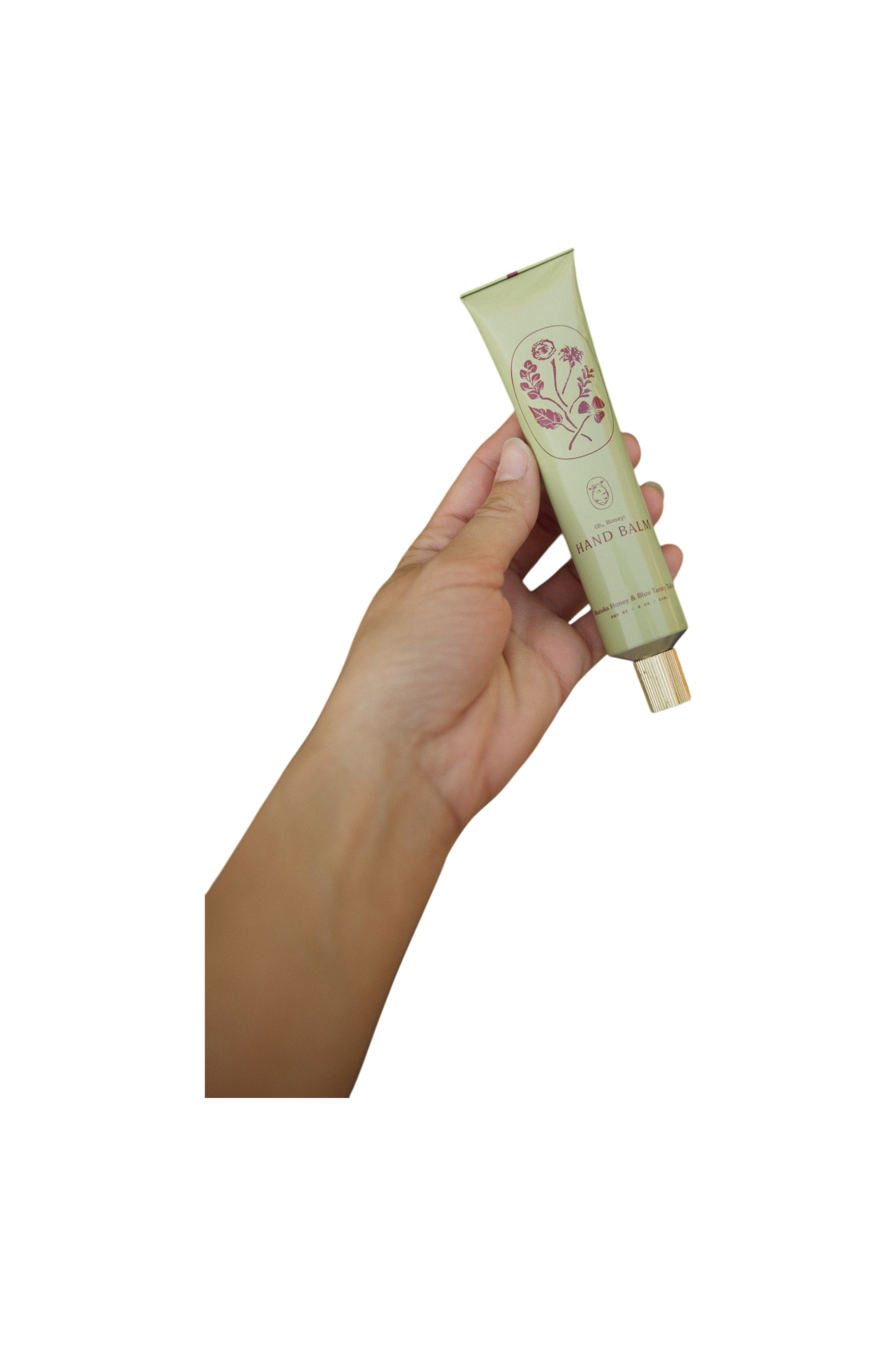 A hand holds a green tube of My Neighbor’s Tallow Manuka Honey & Blue Tansy Tallow Hand Cream with a gold cap and floral label, shown against a black background.