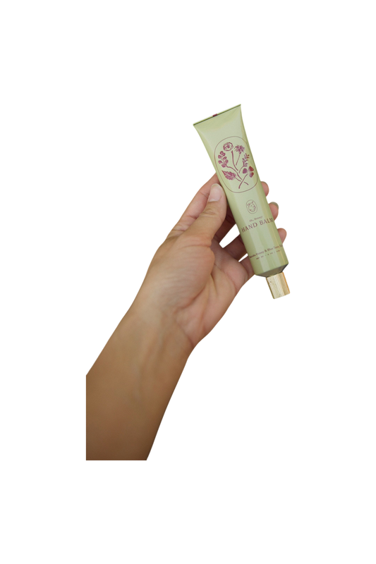 A hand holds a green tube of My Neighbor’s Tallow Manuka Honey & Blue Tansy Tallow Hand Cream with a gold cap and floral label, shown against a black background.