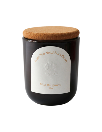 A dark glass jar beeswax candle with a cork lid, labeled "My Neighbor’s Tallow" and "Wild Bergamot Tallow Candle 10 oz," features a subtle floral design and highlights the use of bergamot essential oil.