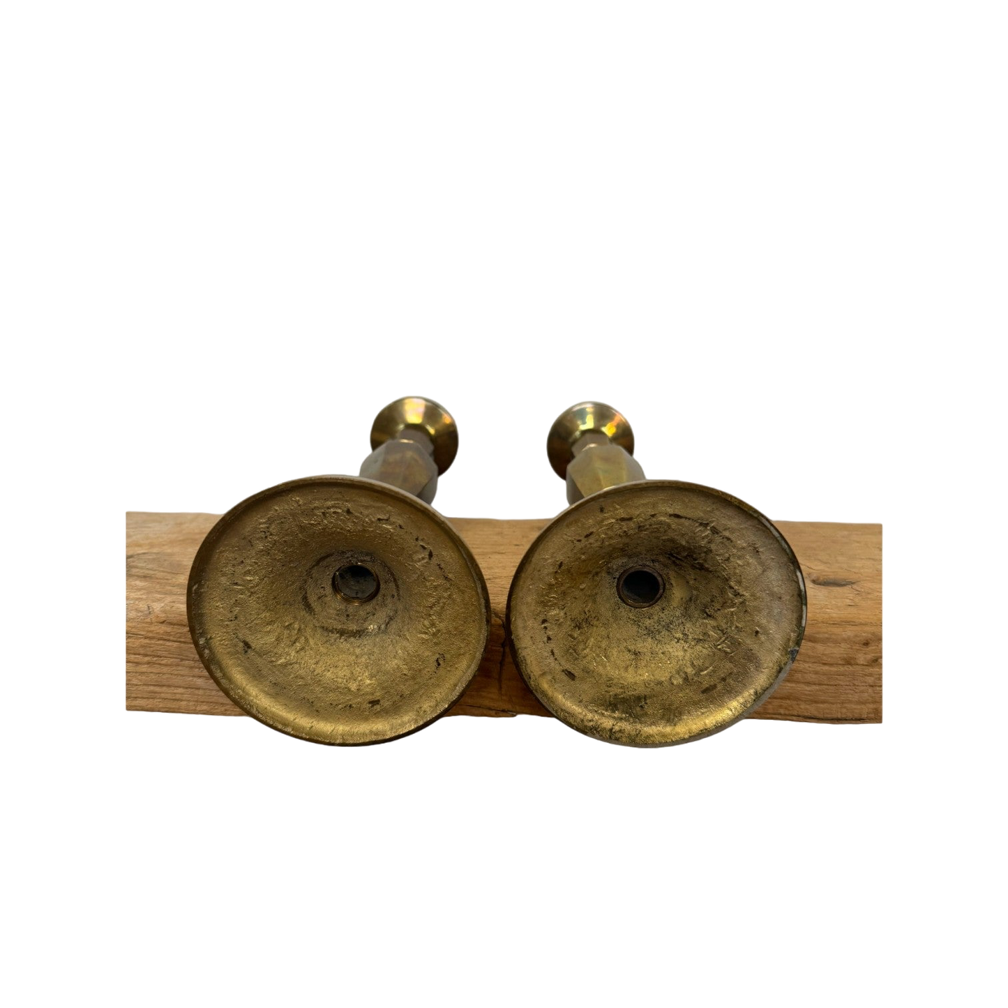 Two Vintage Brass Candle Holders from Shoppe Maison are placed upside down on a wooden beam, showcasing their textured bases against a completely black background that highlights the homewares and wood.