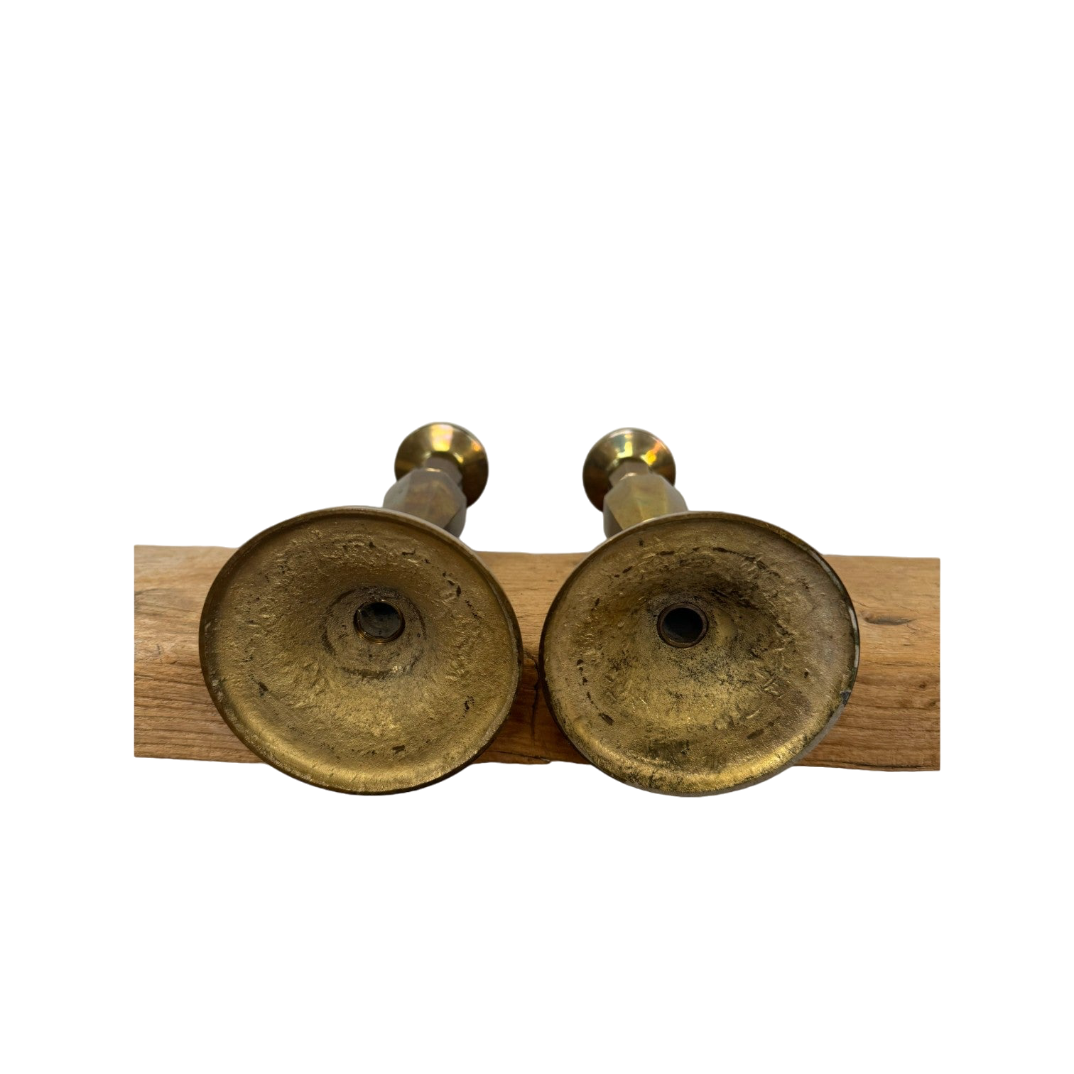 Two Vintage Brass Candle Holders from Shoppe Maison are placed upside down on a wooden beam, showcasing their textured bases against a completely black background that highlights the homewares and wood.
