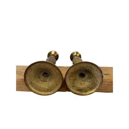 Two Vintage Brass Candle Holders from Shoppe Maison are placed upside down on a wooden beam, showcasing their textured bases against a completely black background that highlights the homewares and wood.