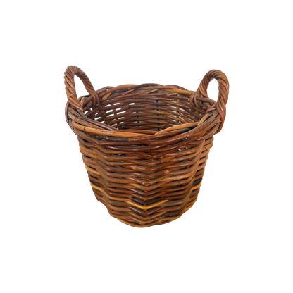The Vintage Woven Basket with Handles from Shoppe Maison is a round, slightly tapered basket made of natural brown rattan. It features two looped handles on either side and boasts a tight, uniform weave.