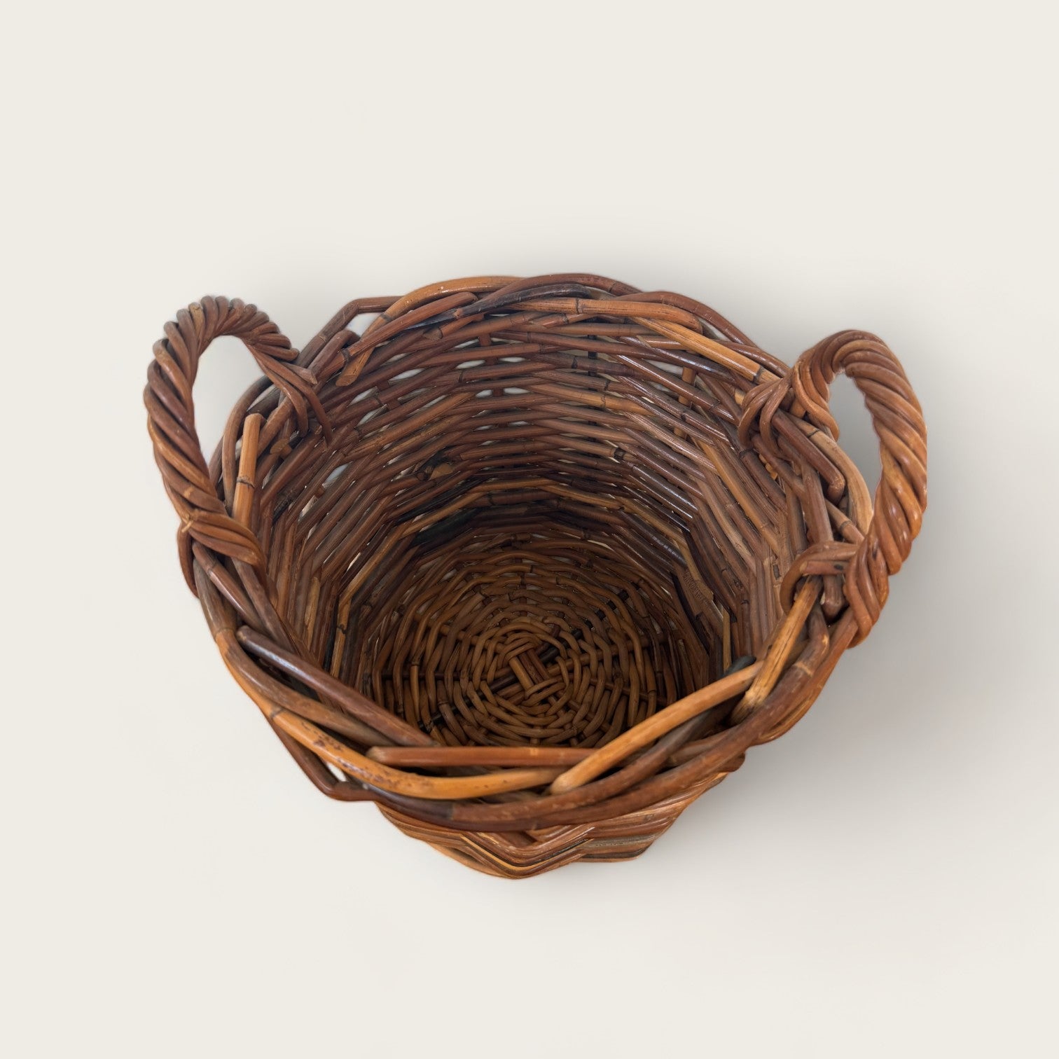 A top-down view of an empty, Vintage Woven Basket with Handles from Shoppe Maison. This charming piece features a rustic appearance and is set against a plain, light background, perfect for your home decor needs.