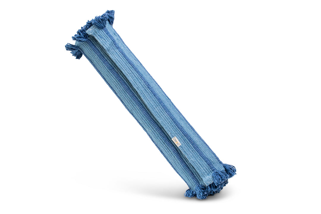 A long, textured yoga mat in an indigo blue hue crafted from organic cotton with tassels on each end, designed for yoga and meditation practices. Its superior grip holds it upright against a plain white background.