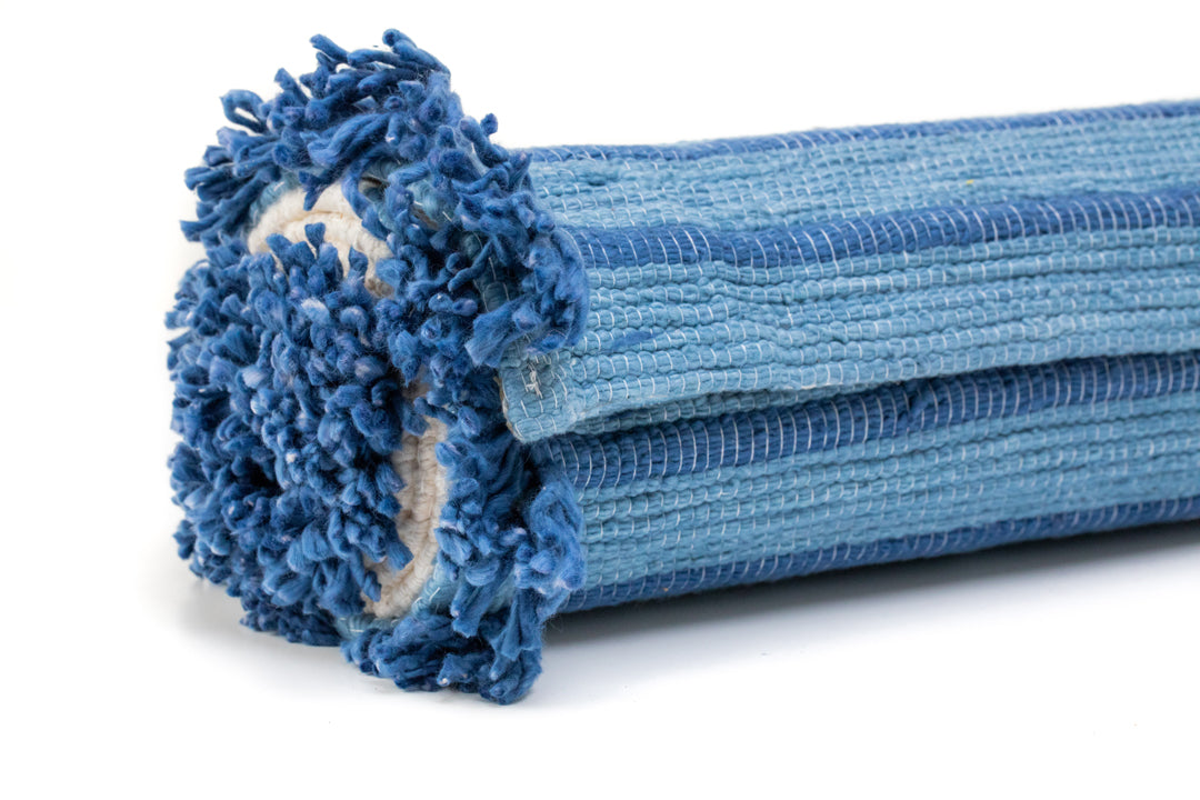 A detailed view of the rolled-up Indigo Ayurvedic Yoga Mat from Bennd Yoga highlights its exceptional grip, with textured loops along the edges. Displaying various shades of blue, this mat presents a soft and inviting look. The close-up of the rolled end emphasizes its material and texture.