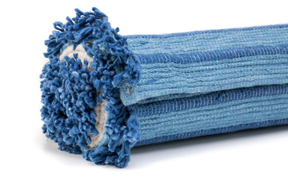 A detailed view of the rolled-up Indigo Ayurvedic Yoga Mat from Bennd Yoga highlights its exceptional grip, with textured loops along the edges. Displaying various shades of blue, this mat presents a soft and inviting look. The close-up of the rolled end emphasizes its material and texture.