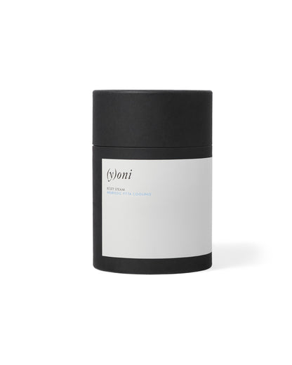 The (y)oni Reset Steam from Surya comes in a cylindrical black container with a white label. It features the words "(y)oni," "RESET STEAM," and "AYURVEDIC PITTA COOLING." This minimalistic, modern design is curated for yoni steam treatments to promote balance within the reproductive ecosystem using Ayurvedic herbs.