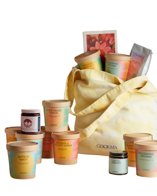 The Cookma Mama Bundle features a yellow tote bag surrounded by colorful food containers, jars, and packets of nourishing postpartum meals, all neatly arranged against a white background.