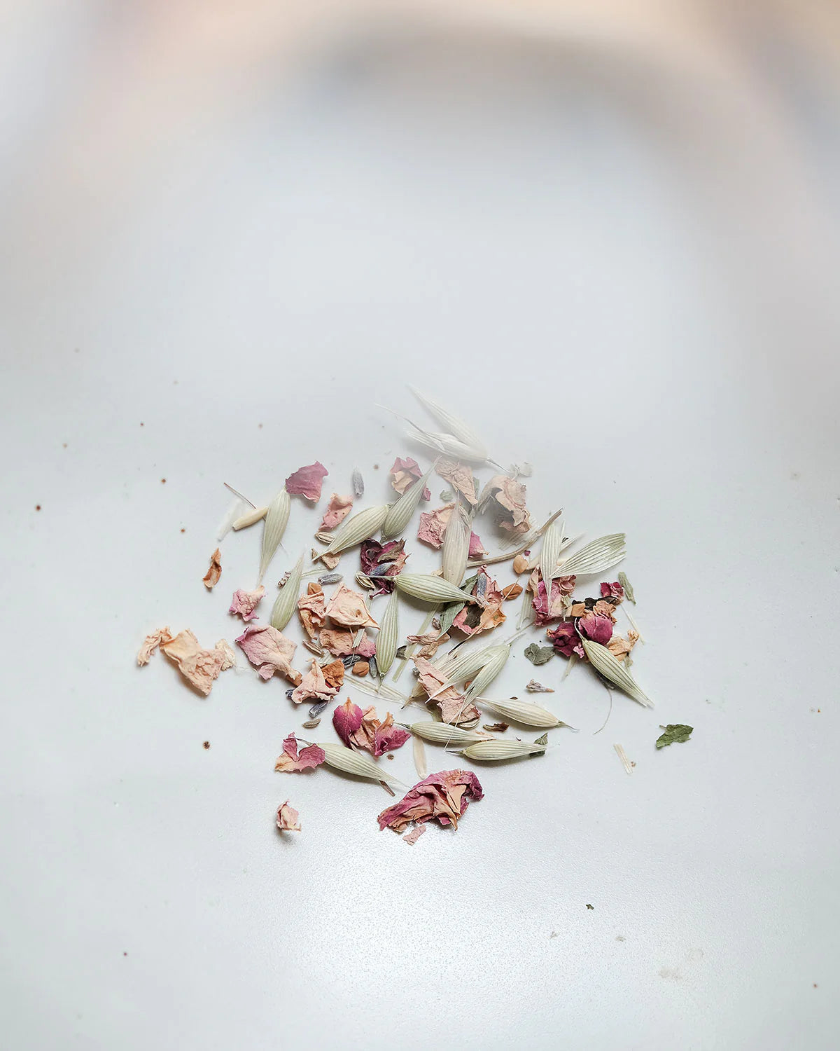 A small pile of dried flower petals and leaves on a white surface reflects the gentle care of Cookma’s Mama Bundle, designed to nourish and support new mothers’ well-being.