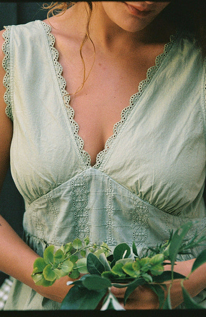 Mint - Wearing the LA RELAXED Makinna Poplin Dress in light green with lace trim, a person holds a bunch of green leaves. Their face is partly out of frame, with hair over one shoulder, keeping attention on the dress and foliage.