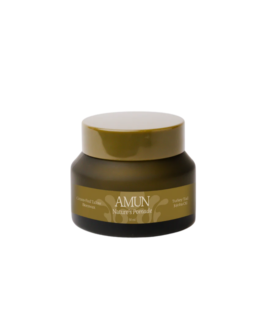 A small, olive-green jar labeled "NATURE’S POMADE" by Amun Organics rests on a white background. Its label highlights beeswax and turkey tail reishi chai as key ingredients for natural hair styling and nourishment.