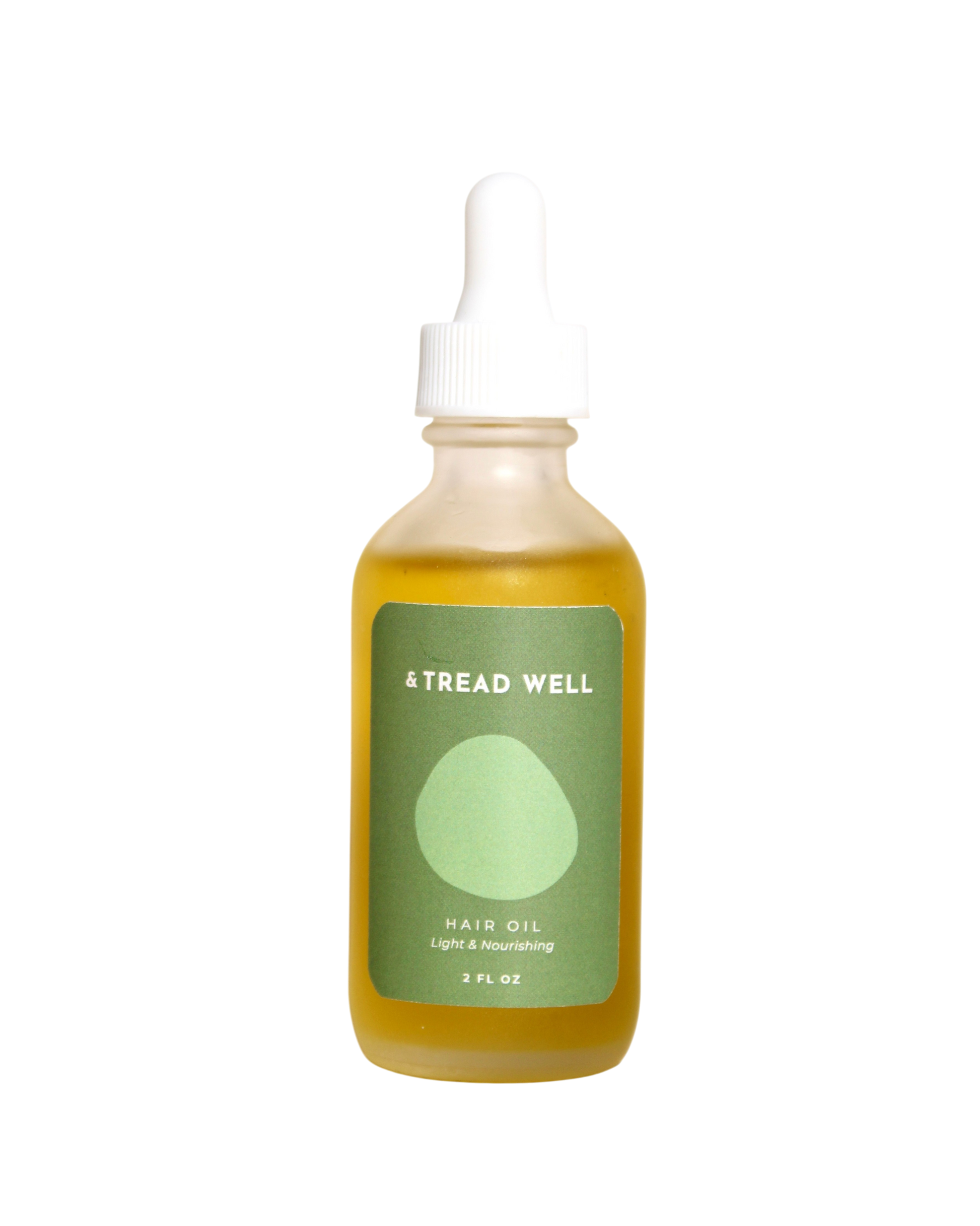 A clear glass dropper bottle with yellow Hair Oil from & Tread Well, featuring a green label that reads “HAIR OIL Light & Nourishing 2 FL OZ”—perfect for scalp treatment.