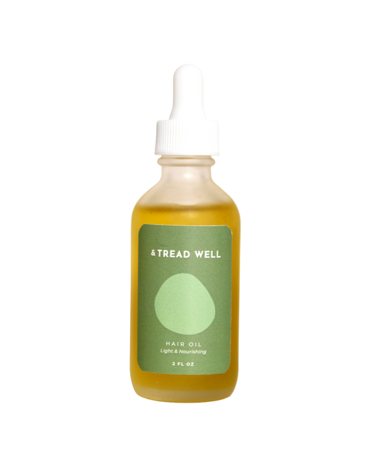A clear glass dropper bottle with yellow Hair Oil from & Tread Well, featuring a green label that reads “HAIR OIL Light & Nourishing 2 FL OZ”—perfect for scalp treatment.