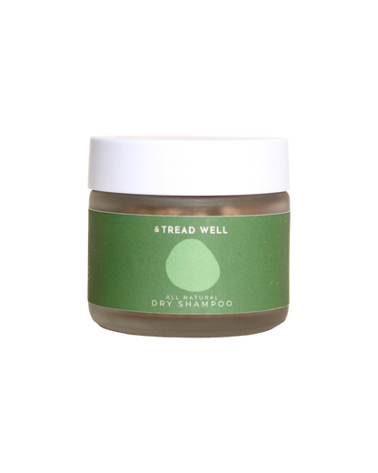 A small clear jar with a white lid and a green label reading "& Tread Well Dry Shampoo." This non-aerosol, plant-based hair powder from & Tread Well features a simple leaf or droplet graphic on its packaging.