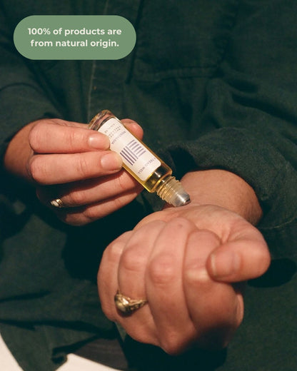 A person applies & Tread Well Natural Fragrance - Nostalgia from a small roller bottle to their wrist. A partially visible label appears, with text: "100% of products are from natural origin and contain pure essential oils.