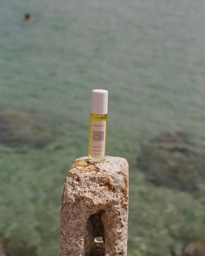 A small bottle of & Tread Well's Natural Fragrance - Nostalgia sits on a weathered stone post by the sea, its pure scent harmonizing with the clear water and rocky shoreline.