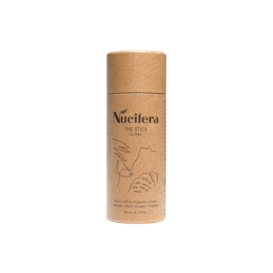 A cylindrical cardboard container labeled "The Stick" from Nucifera Body Store against a black background. The light brown packaging features minimalist illustrations and black text. The label highlights the product as a vegan, multi-purpose balm for skin irritations, containing 60 ml or 2 fl oz.