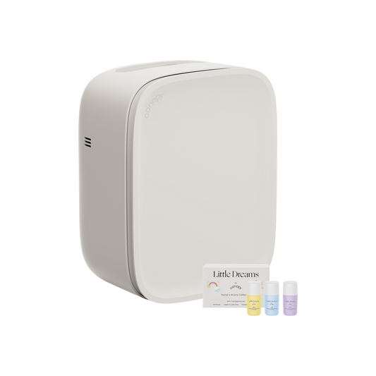 A sleek, white rectangular diffuser with rounded edges sits beside three small essential oil bottles and a "Little Dreams" card, creating a serene nursery vibe. Pair with the Canopy Nursery Air Purifier for ultra-clean air using HEPA-13 filtration.