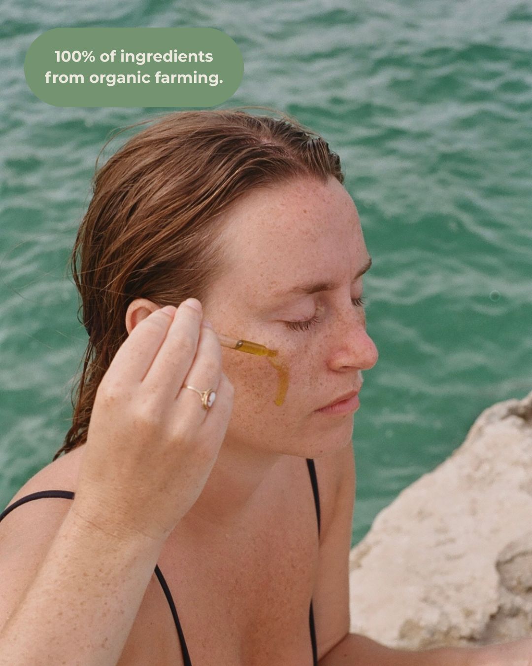 A woman with closed eyes applies & Tread Well Oil Cleanser using a dropper by turquoise water. Above her, text reads: "100% of ingredients from organic farming.