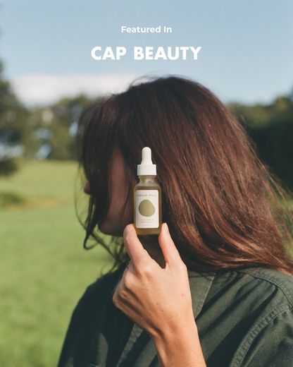 A person with long brown hair holds a dropper bottle labeled "& Tread Well Face Serum" near their face outdoors with trees and grass in the background. The words "Featured In CAP BEAUTY" appear at the top of the image.