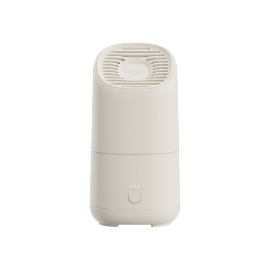 The Canopy Portable Humidifier is a modern, white, cylindrical device with a vented top and a front circular button featuring three indicator lights, shown against a plain white background.