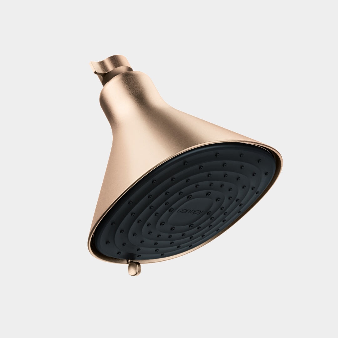The Canopy Filtered Showerhead features a modern metallic gold finish and a matte black spray face, shown angled against a plain light gray background. Seamless delivery and quality assurance provided by Canopy.
