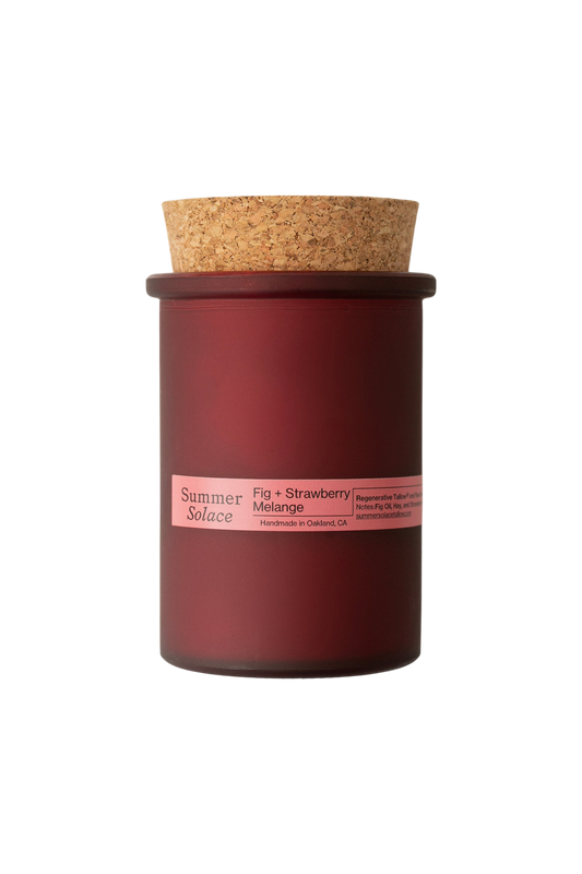 A burgundy glass candle jar with cork lid and pink label reading "Summer Solace, Fig + Strawberry Melange." The 6 oz. Regenerative Tallow® candle by Summer Solace Tallow stands out against a black background. Crafted in Oakland, CA.