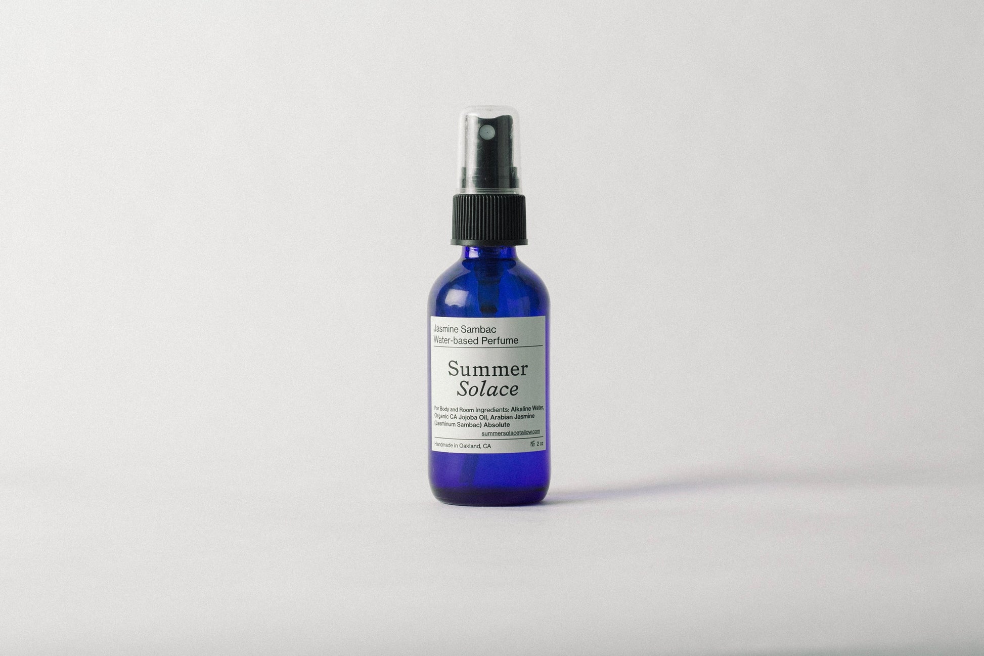 A blue spray bottle of Summer Solace Tallow’s Jasmine Sambac + Magnolia Perfume Mist (Water-Based) UPDATED FORMULA stands upright on a plain white background, with black text highlighting its fresh floral scent and ingredients.
